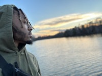 a man in a green hoodie standing by a body of water